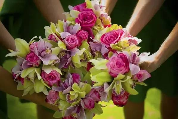 Three bridesmaids holding bouquets of pink roses, green orchids and lavender blooms.