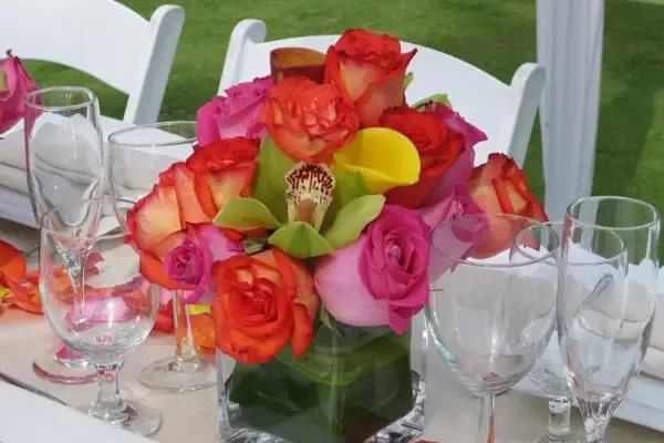 A reception table with a centerpiece of orange roses, calla lilies and pink blooms.
